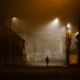 Lonely woman walking in foggy old city with street lights in a coat